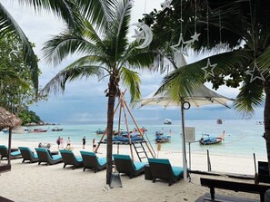 A beach with lounge chairs, a thatched-roof structure, and boats in the water.