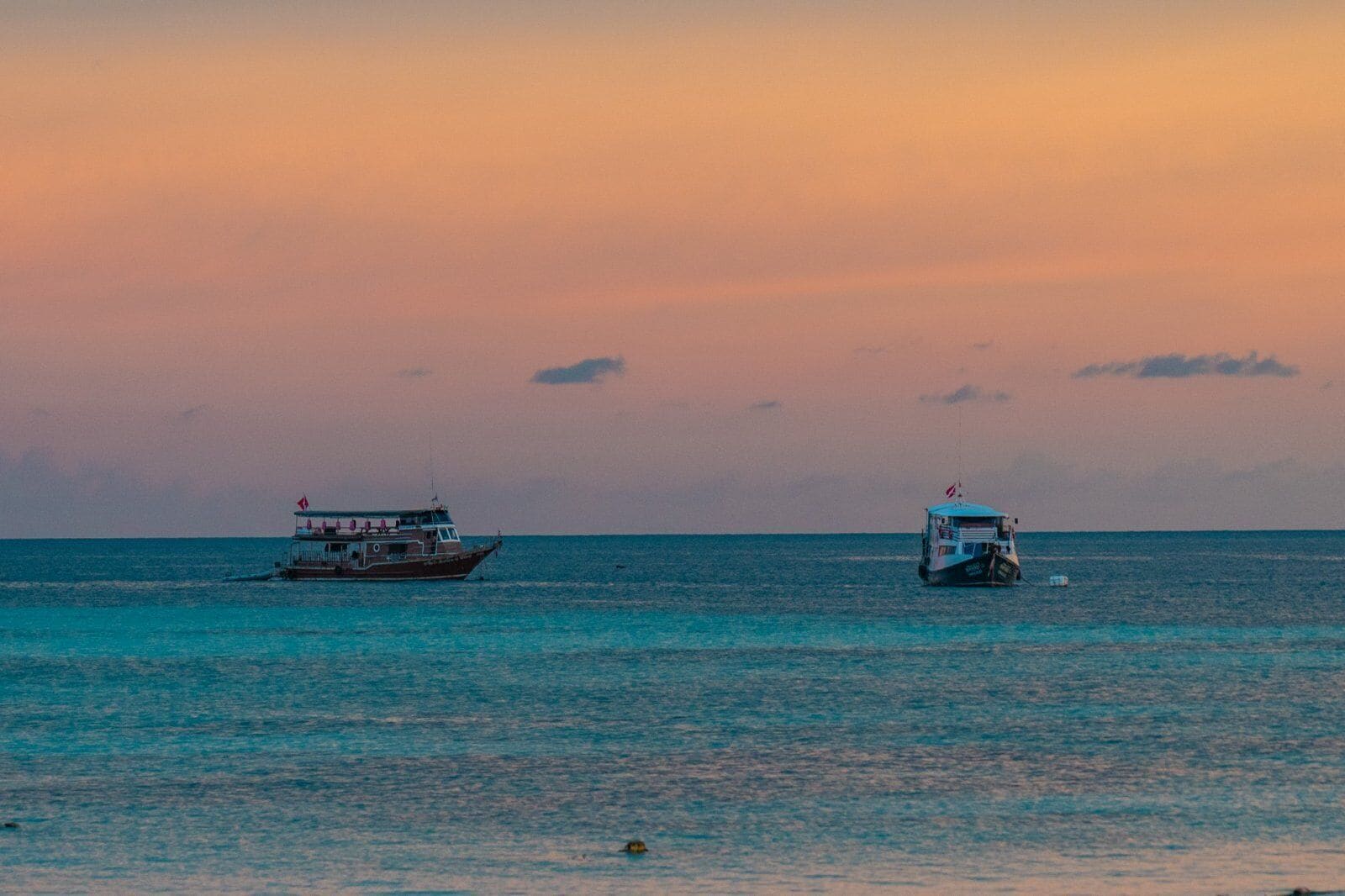 Two boats on calm sea water during sunset.