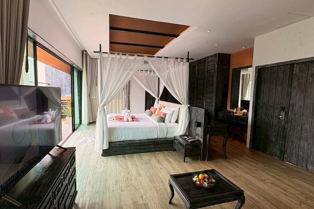 A bedroom with a bed, a TV, a bedside table, a coffee table with fruit, and a large window.