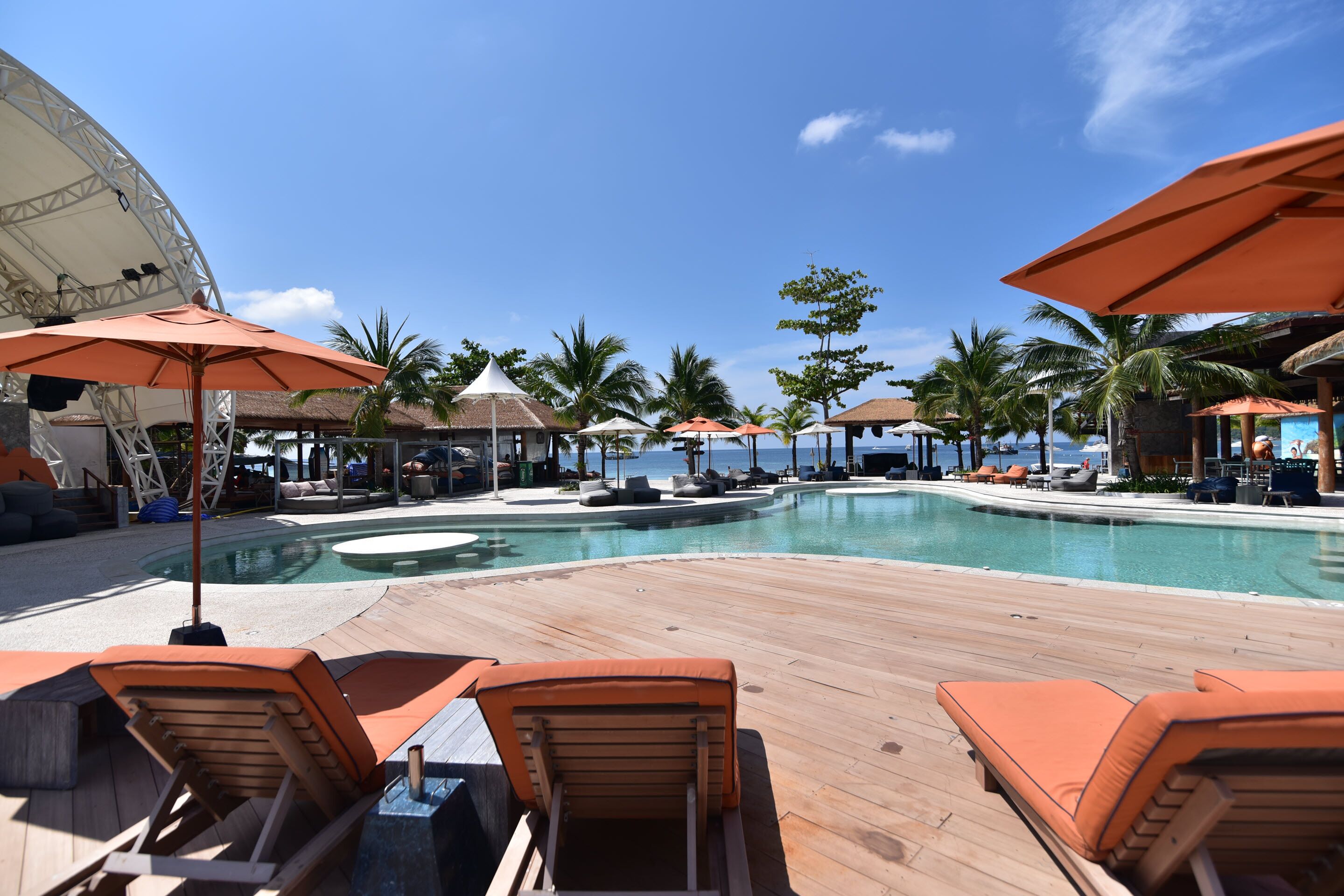 A poolside area with lounge chairs and umbrellas, a large pool, and a view of the ocean.