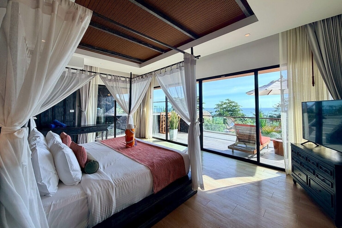 A bedroom with a bed, curtains, a TV, and a balcony with a view.