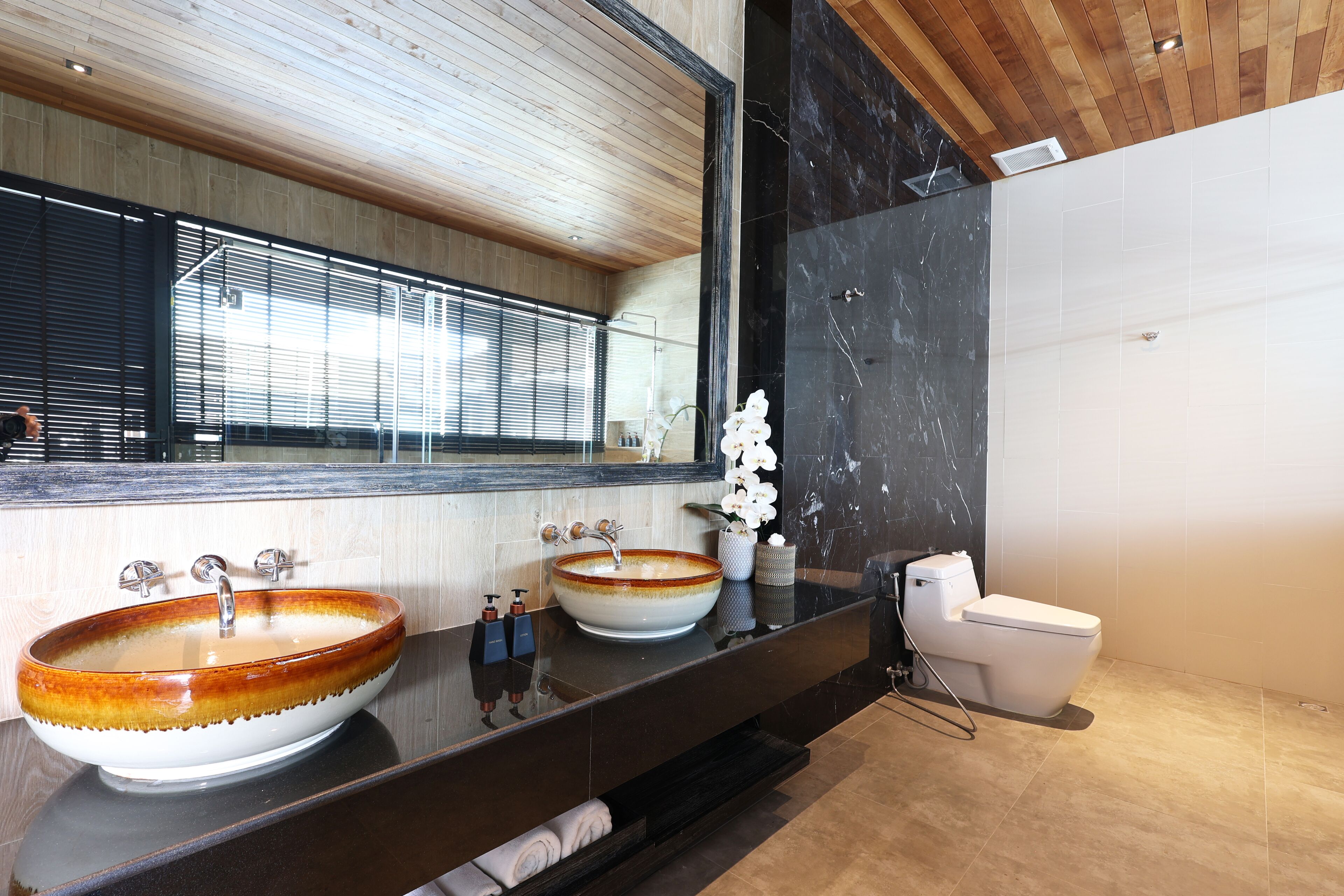 A modern bathroom with two large ceramic sinks, a toilet, and a large mirror.