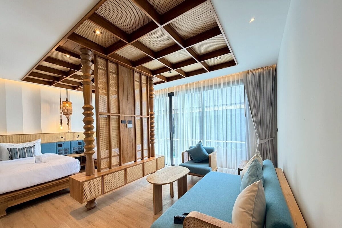 A hotel room with a bed, a sofa, a small table, and a partition with a woven design.