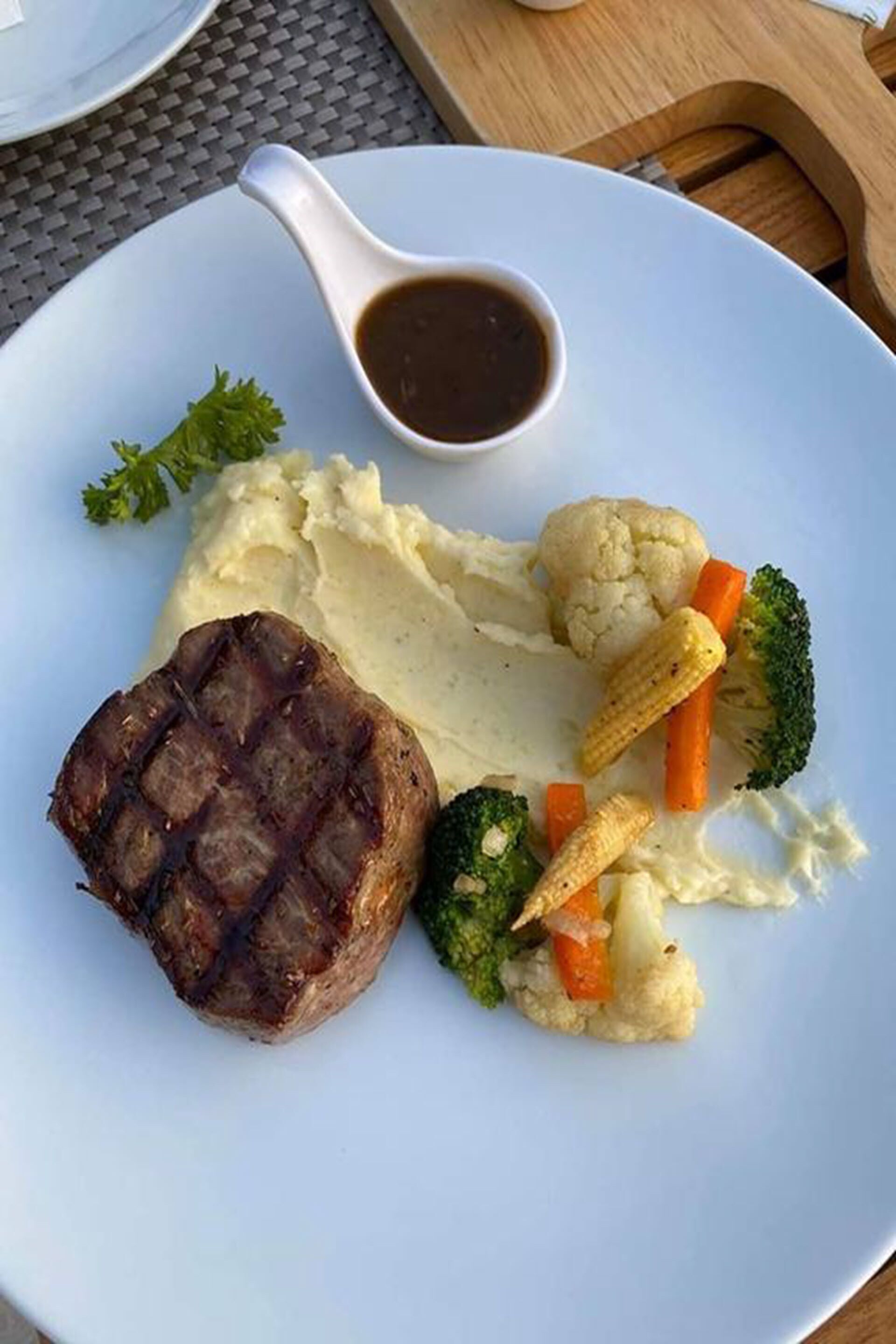 Un plato con bistec a la parrilla, puré de papas y verduras al vapor, incluyendo brócoli y zanahorias.