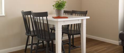 Un comedor con una mesa blanca y cuatro sillas negras, una planta en maceta sobre la mesa y piso de madera.