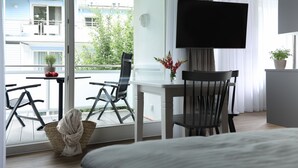 A hotel room with a balcony, a TV, a dining table, and chairs. - Villa am Park (Binz)
