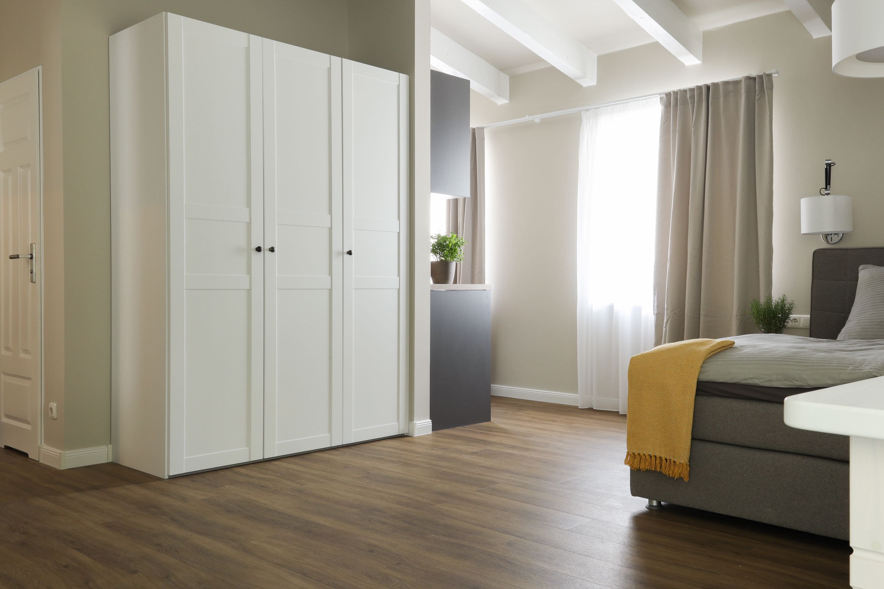 A bedroom with a bed, a wardrobe, a window with curtains, and a bedside lamp.