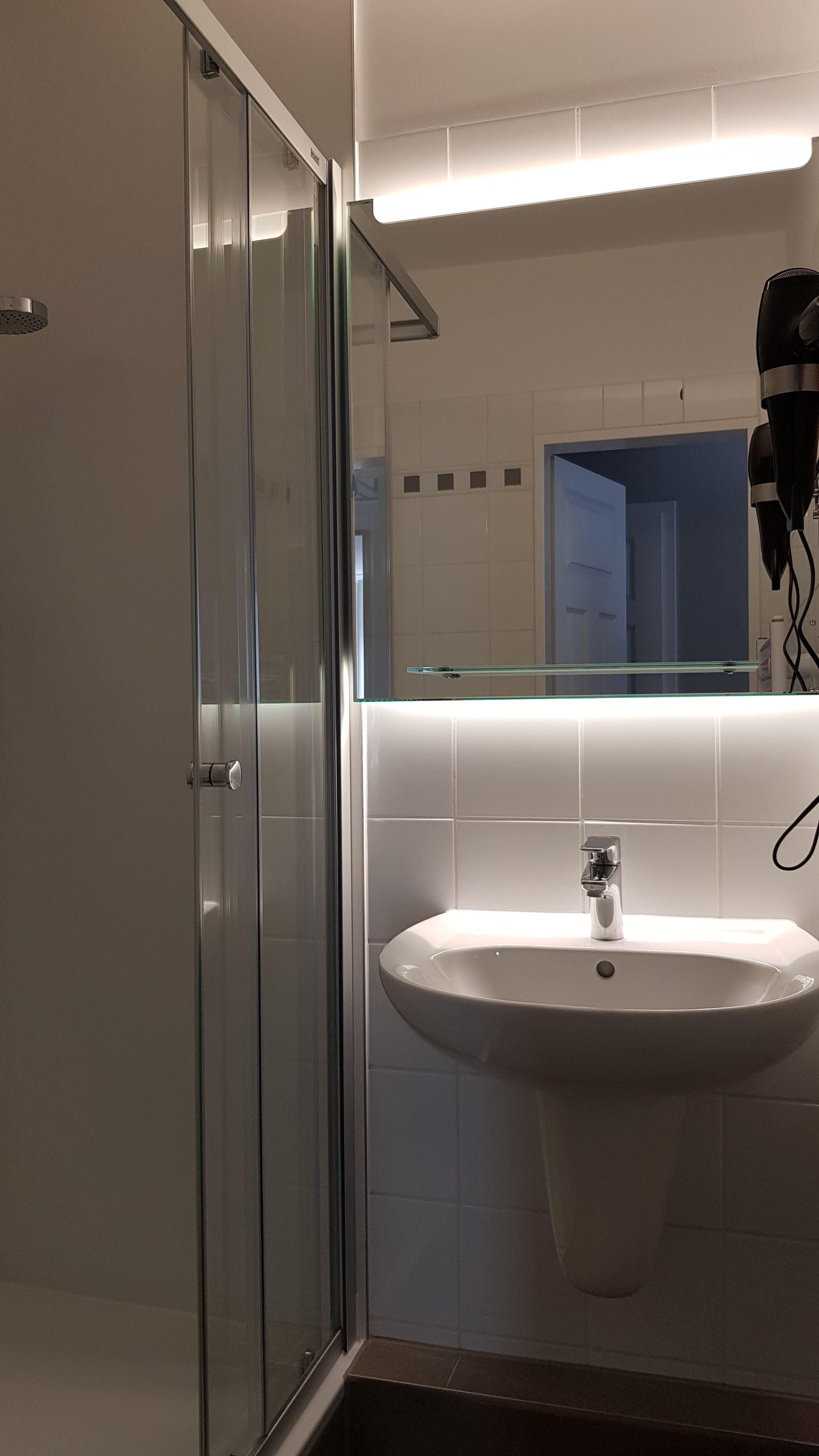A modern bathroom with a glass shower enclosure, a white sink, and a mirror above the sink.