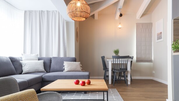 A modern living room with a sectional sofa, a wooden coffee table, and a dining area with a table and chairs. - Villa am Park (Binz)
