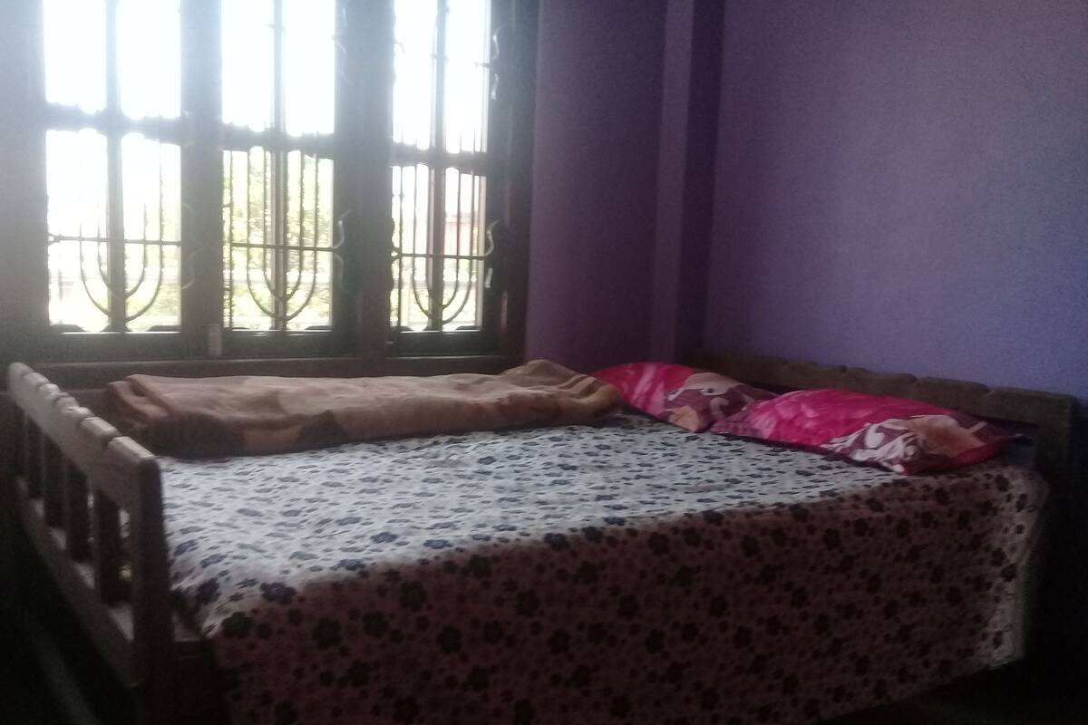 A small room with a bed, a window with metal bars, and purple walls.