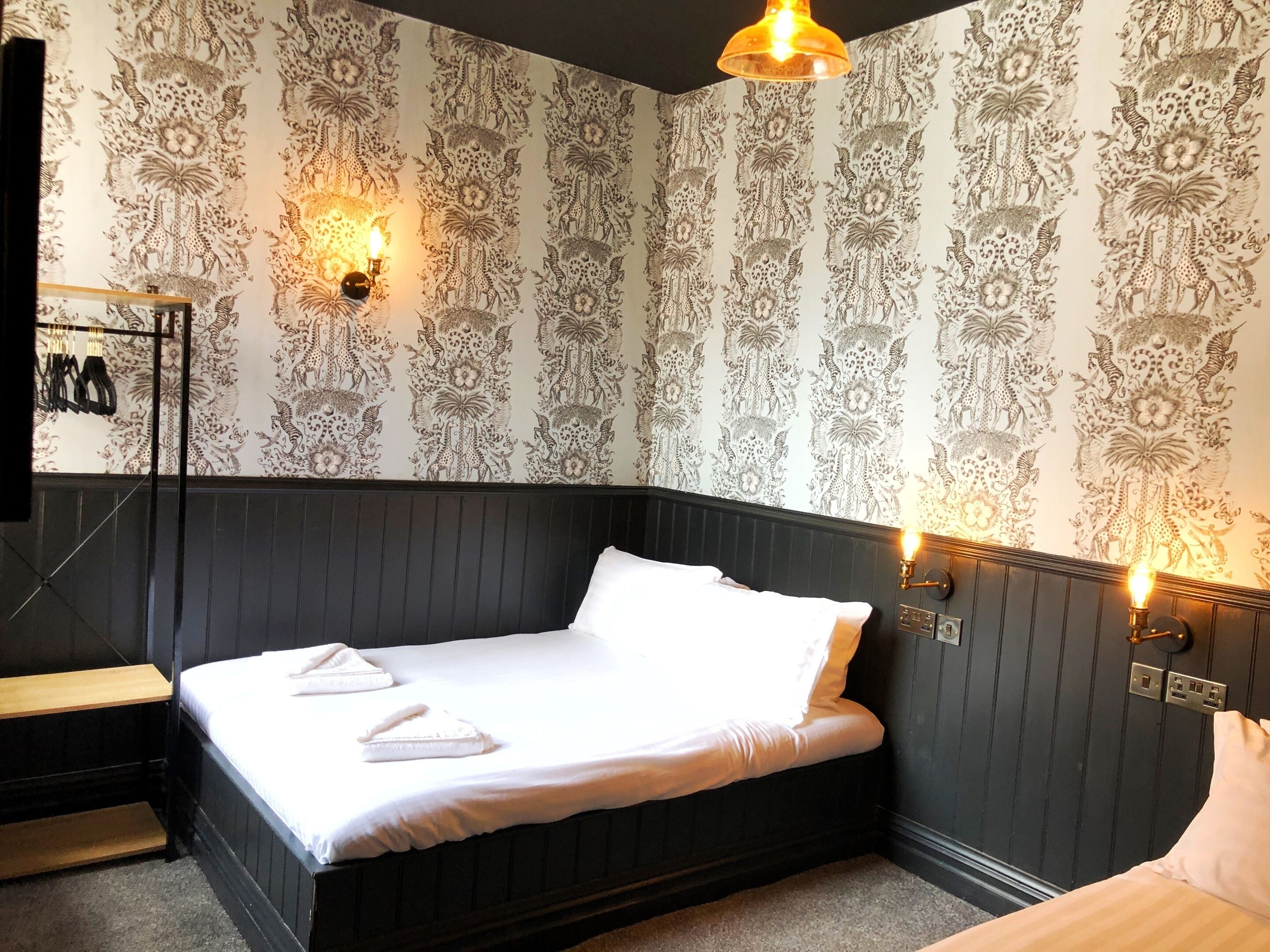 A neatly made bed with white linens and pillows, a dark headboard, and a wall with intricate black and white floral wallpaper.