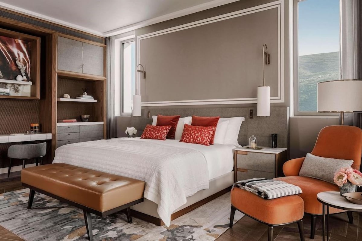 A modern hotel room with a large bed, a desk, a chair, and a view of the city.