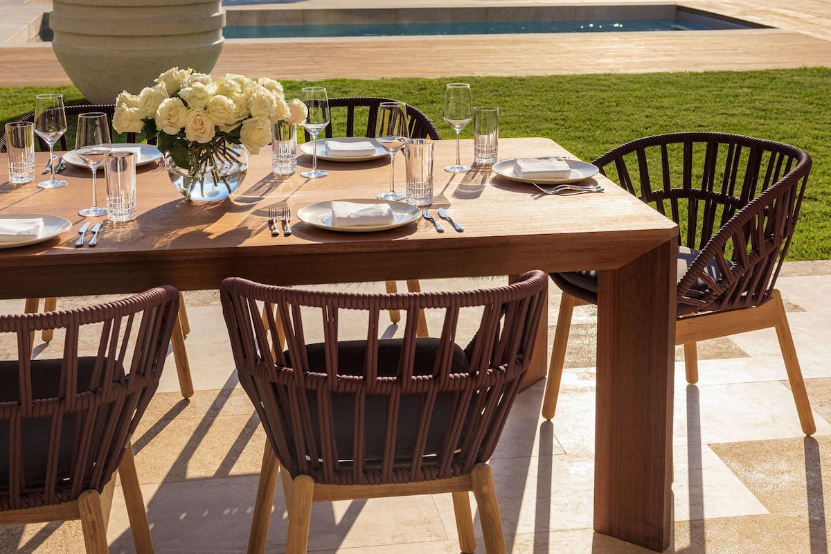 An outdoor dining area with a table set for four, chairs, a potted plant, and a view of the sea.