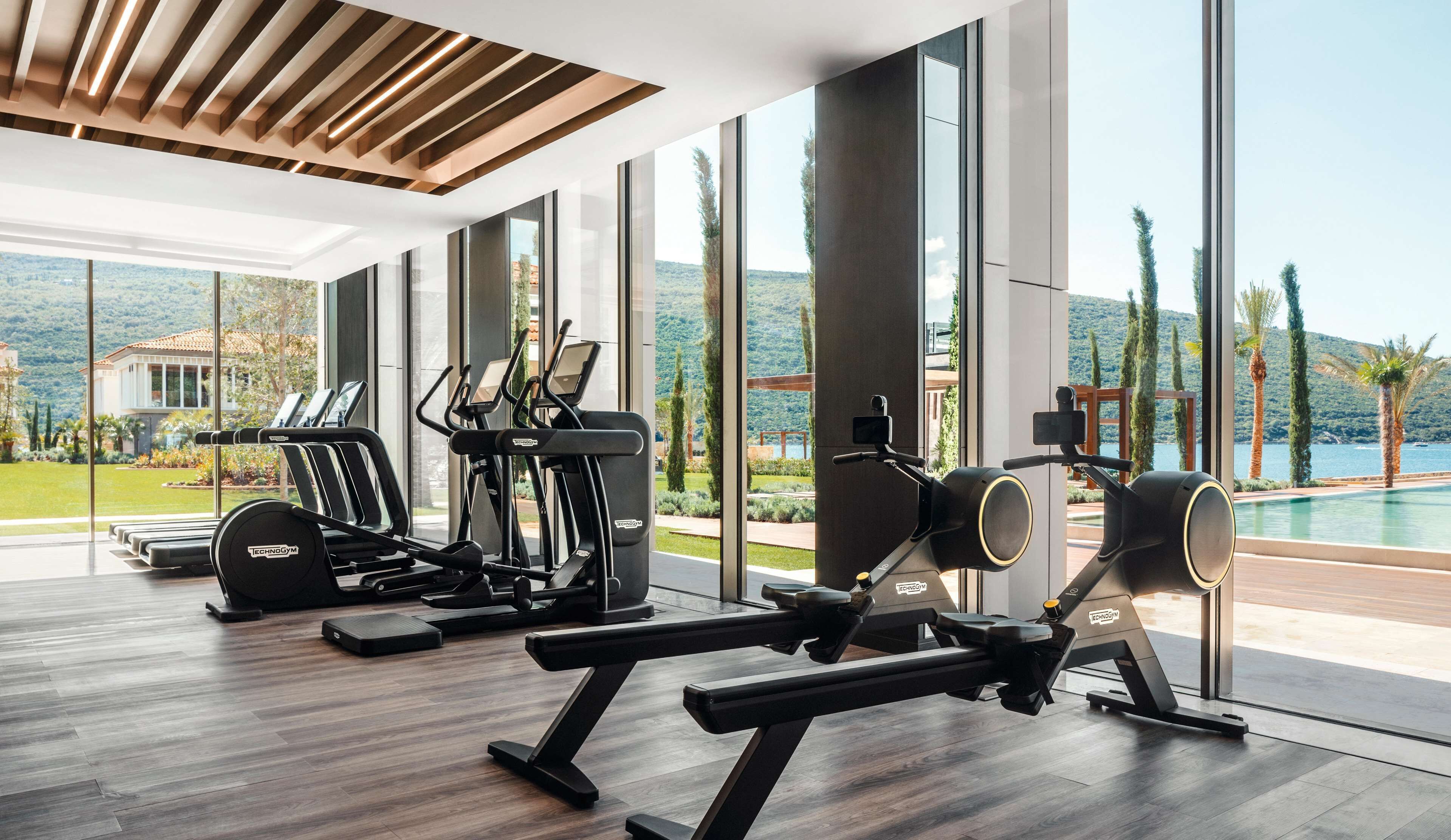 A modern gym with cardio machines, weightlifting equipment, and large windows offering scenic views.