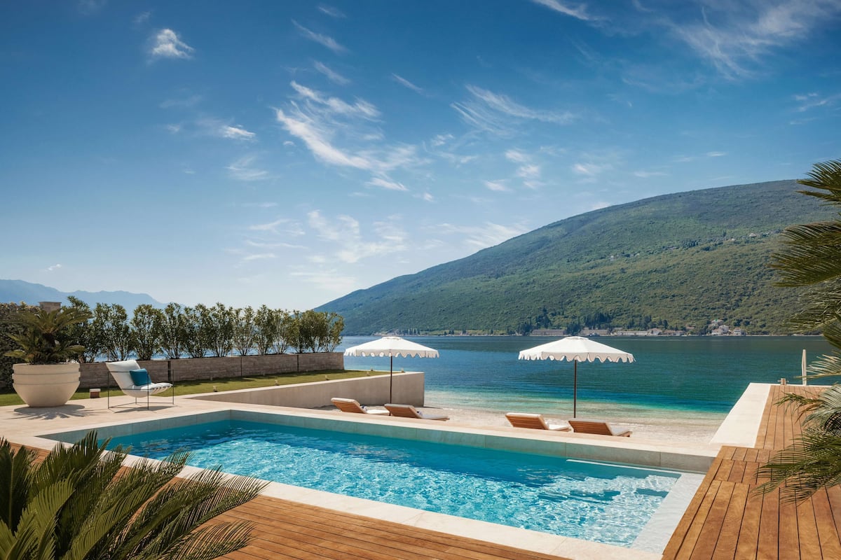 A swimming pool with lounge chairs and umbrellas, overlooking a lake and mountains.