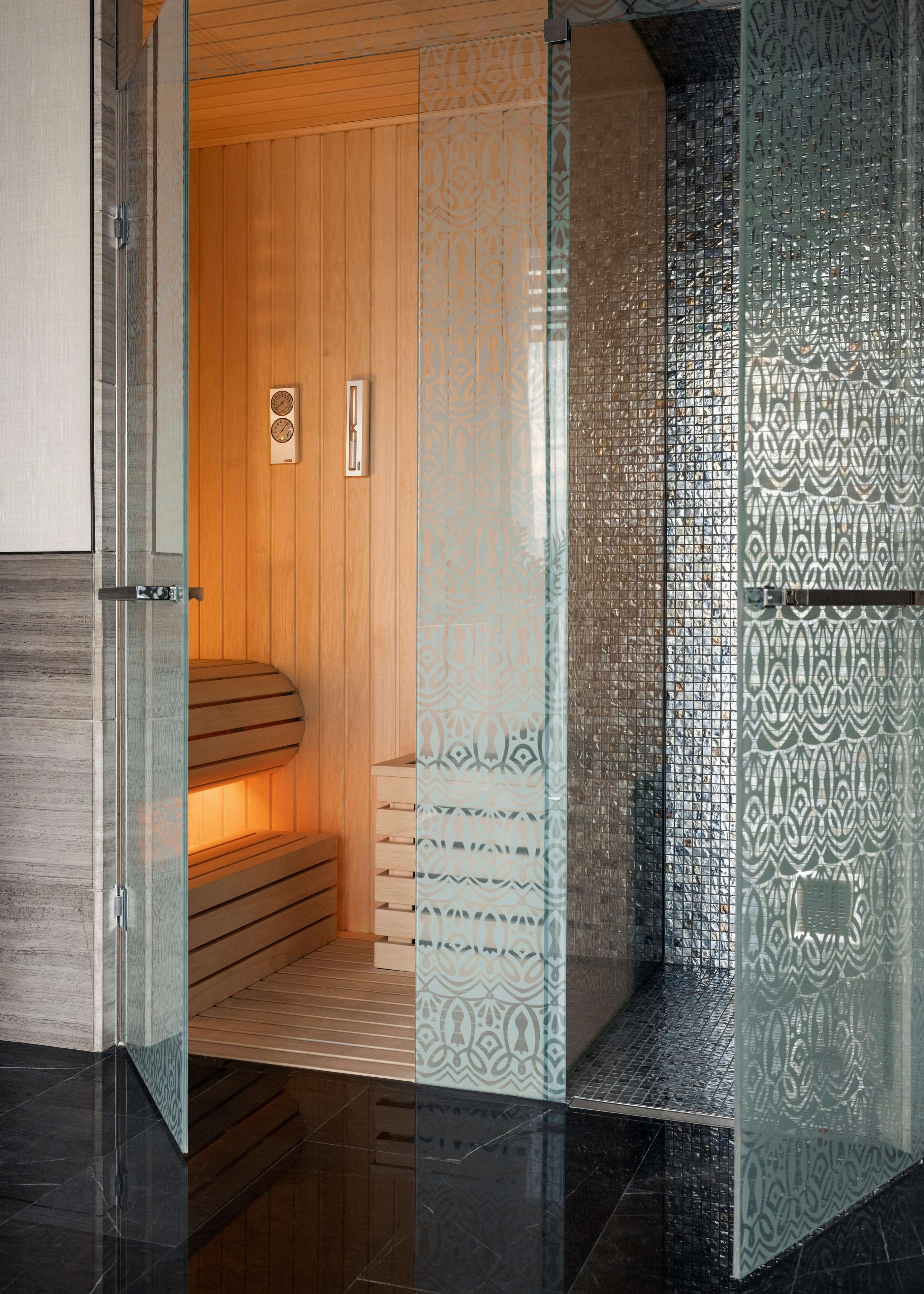 A sauna with wooden benches, a glass door, and patterned glass panels.
