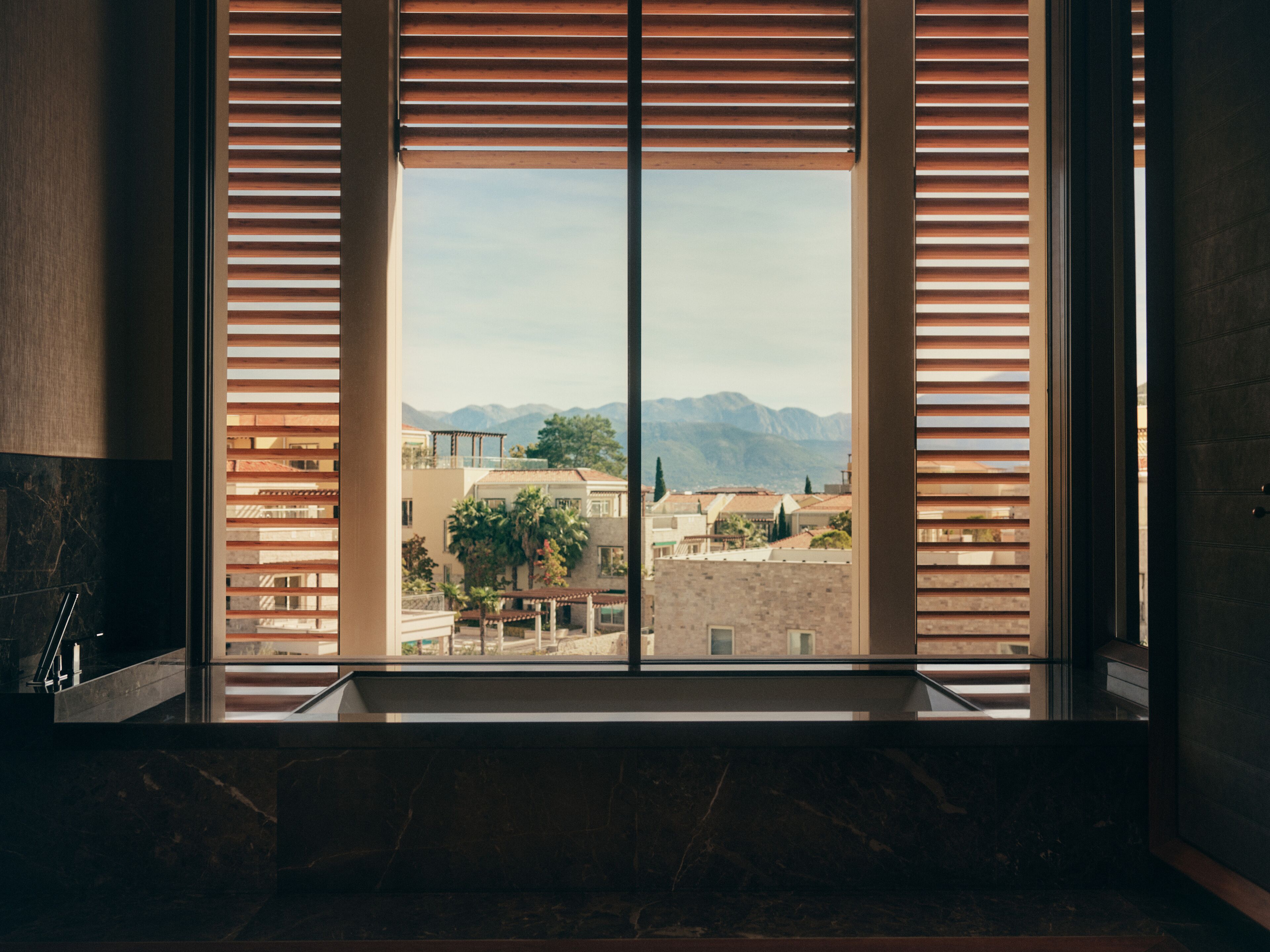 A bathroom with a large window, a marble sink, and a view of buildings and mountains.