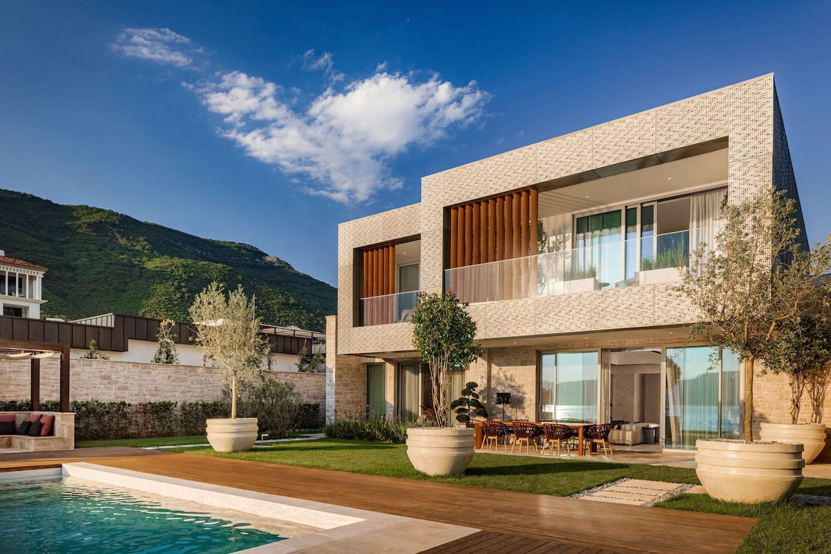 A modern two-story house with a swimming pool, outdoor seating, and a mountain backdrop.