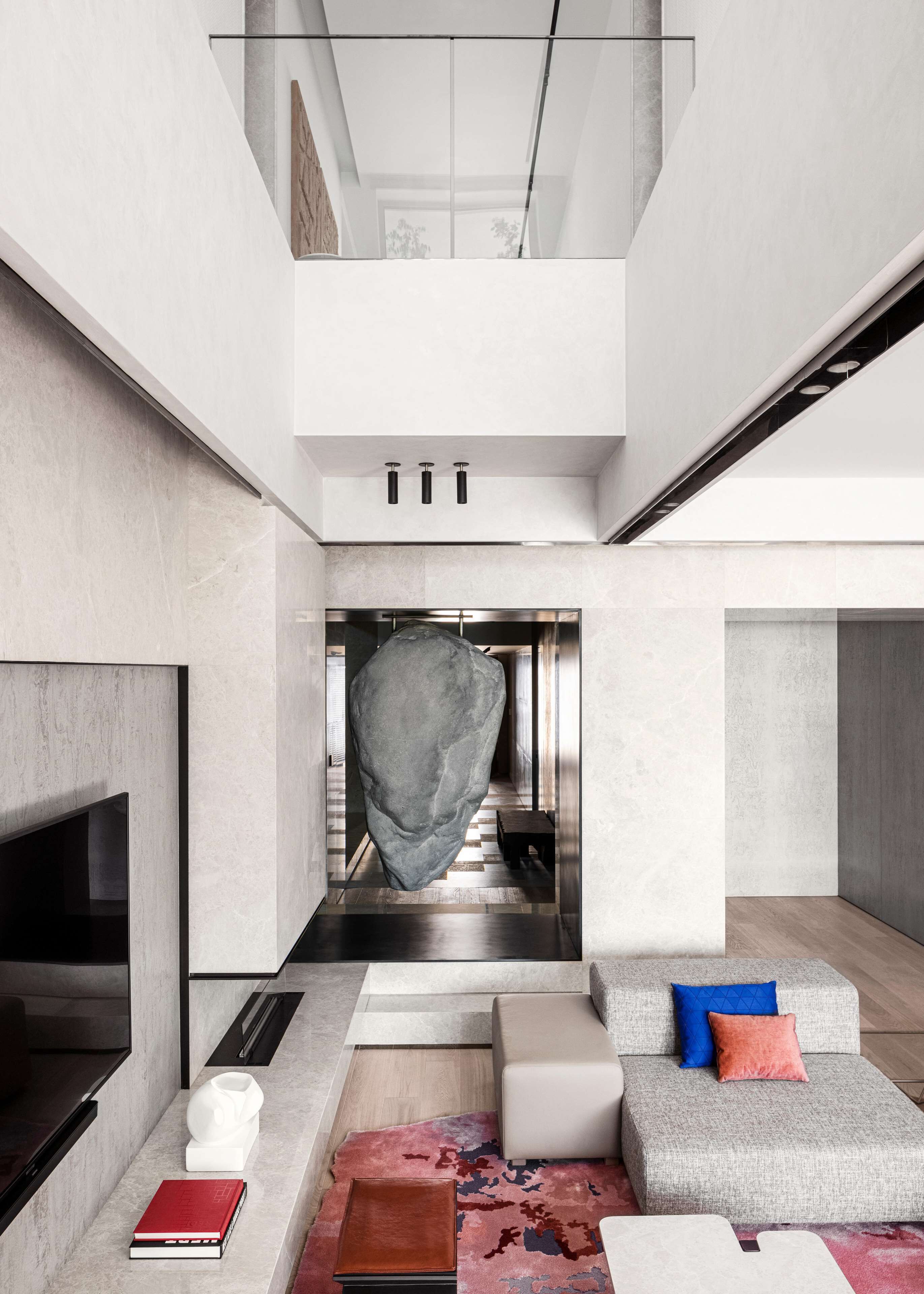 A modern interior with a large stone sculpture, a flat-screen TV, a sofa with cushions, and a patterned rug.