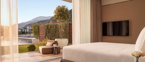 A modern bedroom with a large bed, a TV, and a view of a landscaped garden and mountains.