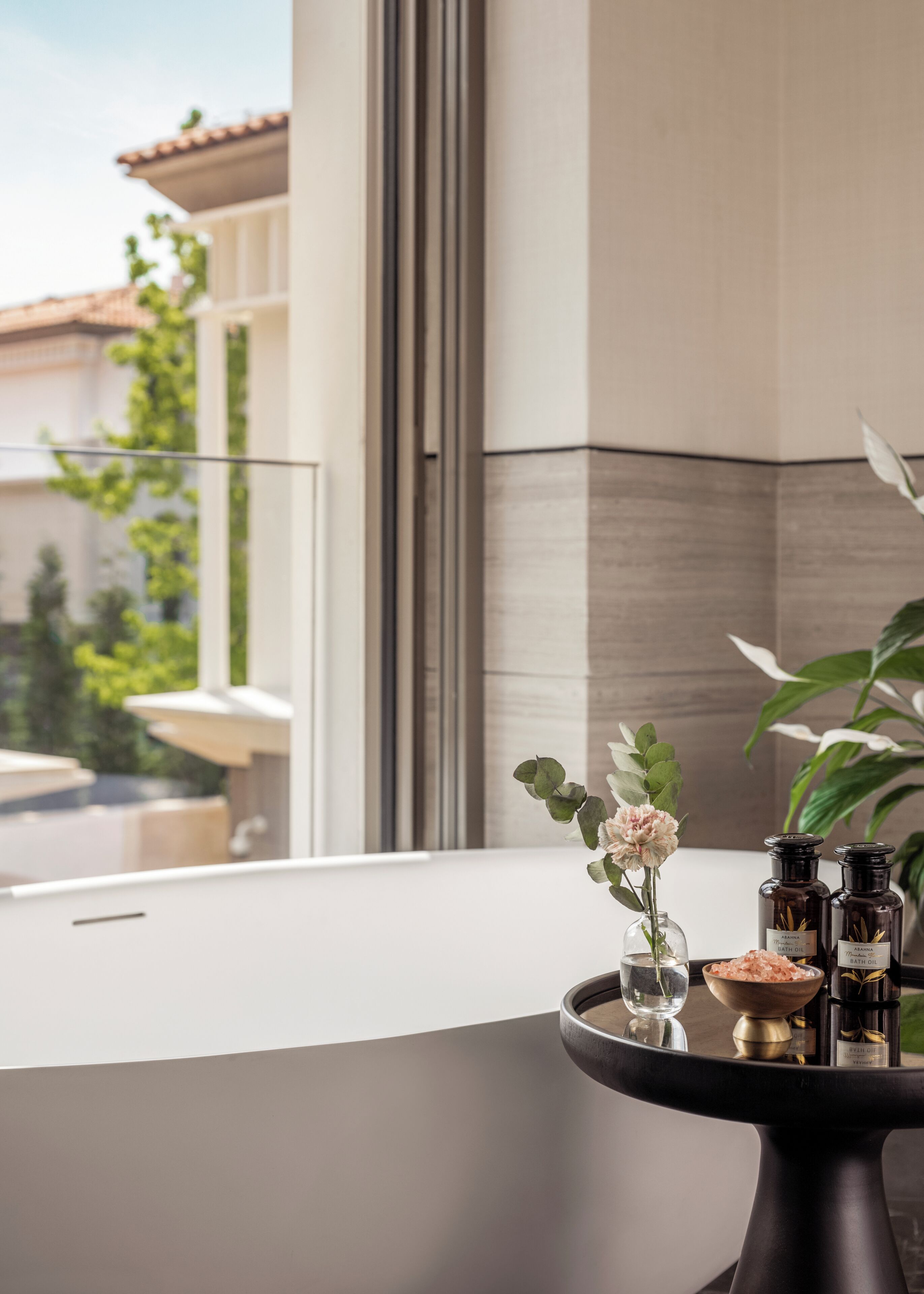 A modern interior with a view of a balcony, a table with a vase of flowers, and two bottles labeled 'AROMA THRASH OIL' and 'AROMA BATH OIL'.