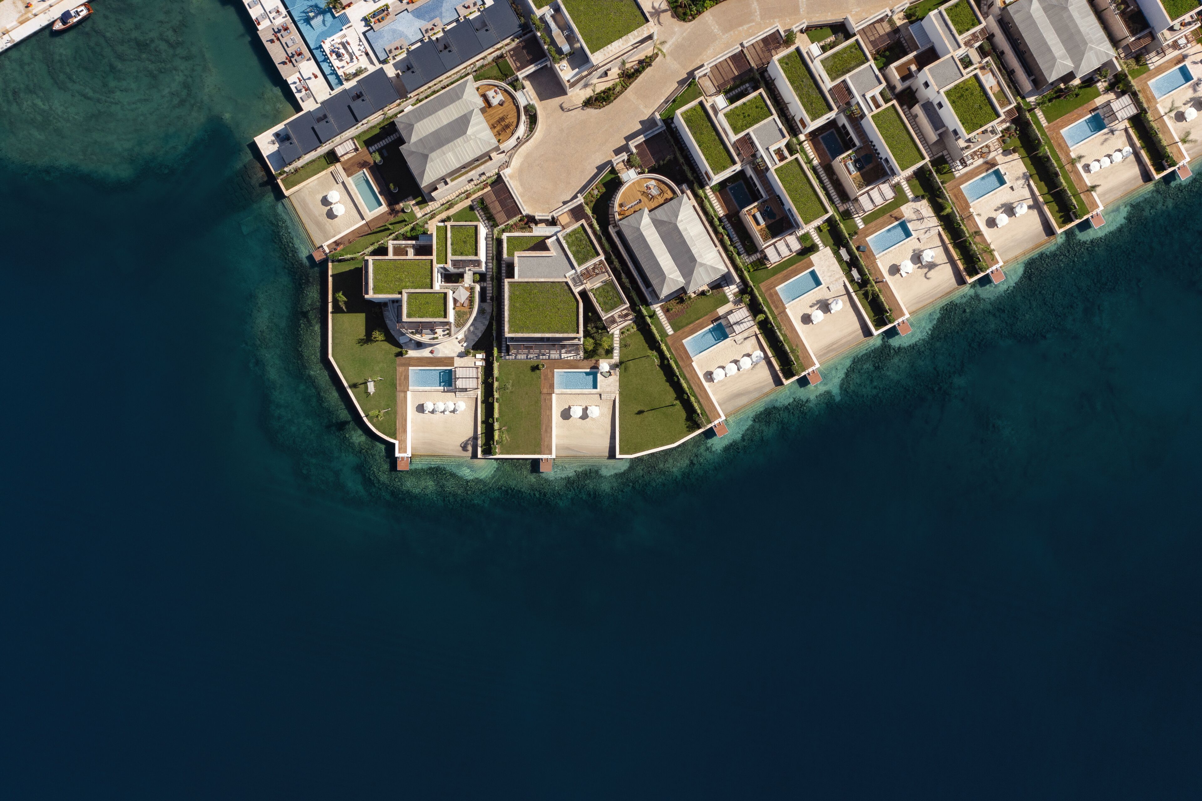 Vue aérienne d’une station balnéaire comprenant plusieurs bâtiments, des piscines et un port de plaisance.