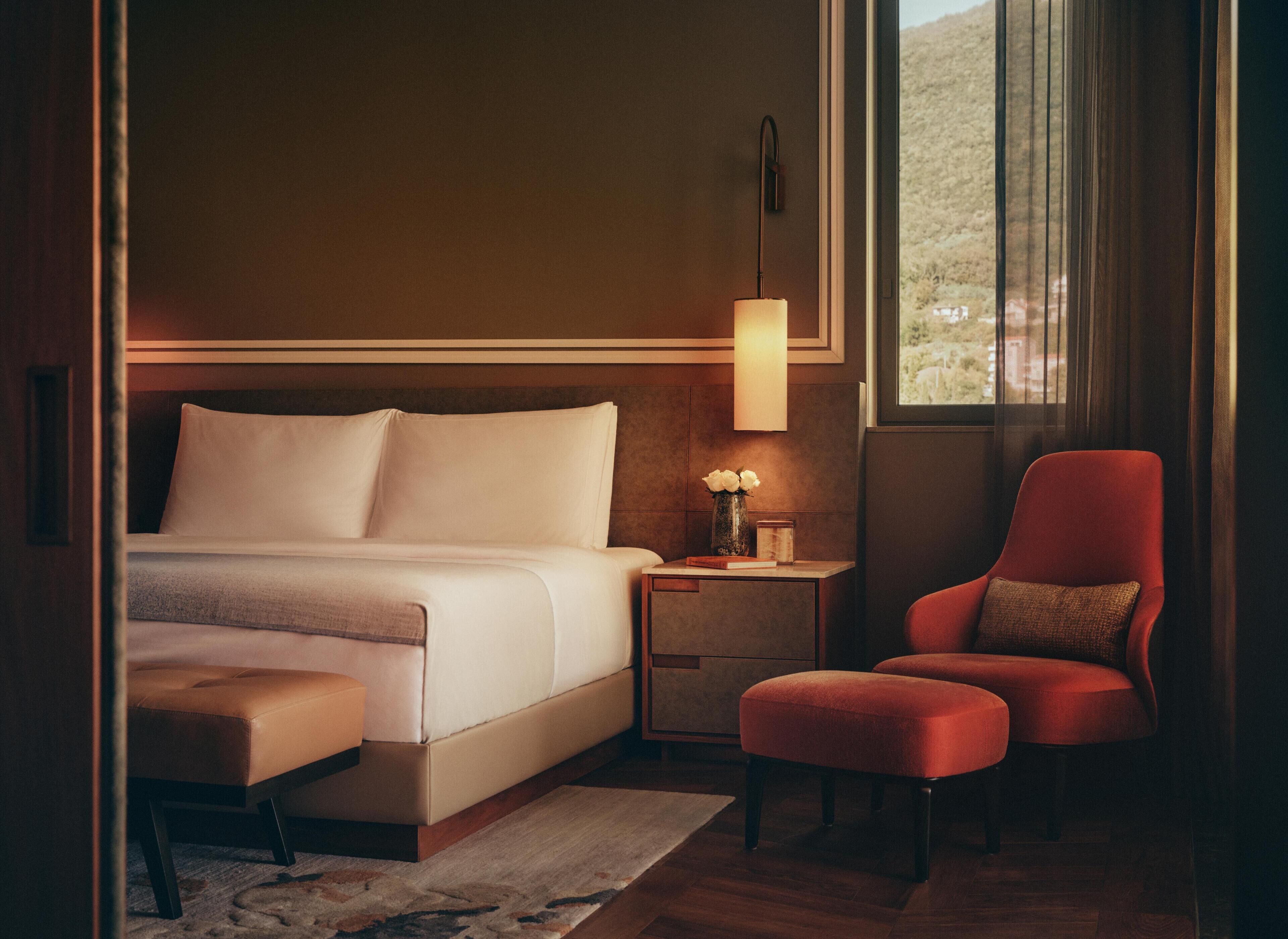 A hotel room with a bed, a nightstand, a chair, and a window.