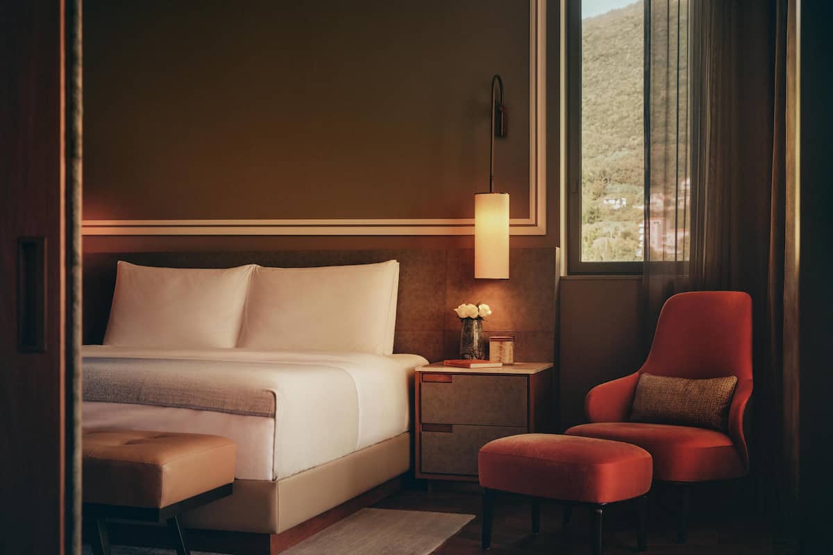 A hotel room with a bed, a nightstand, a chair, and a window.