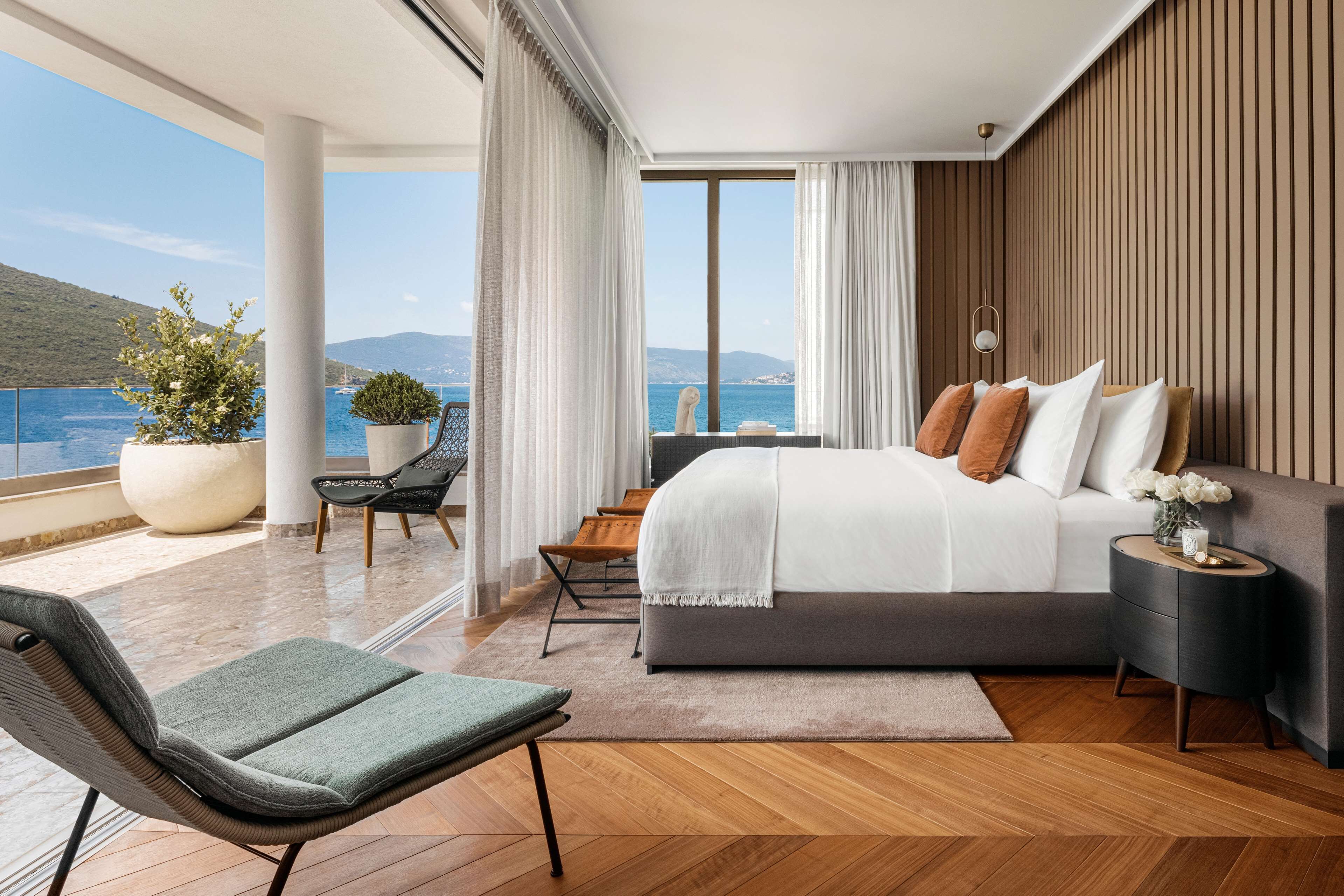 A modern bedroom with a large bed, a view of the sea, and a balcony with seating.