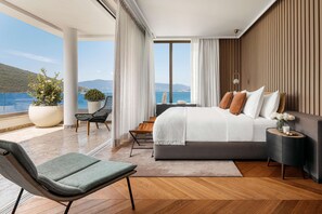 A modern bedroom with a large bed, a view of the sea, and a balcony with seating.