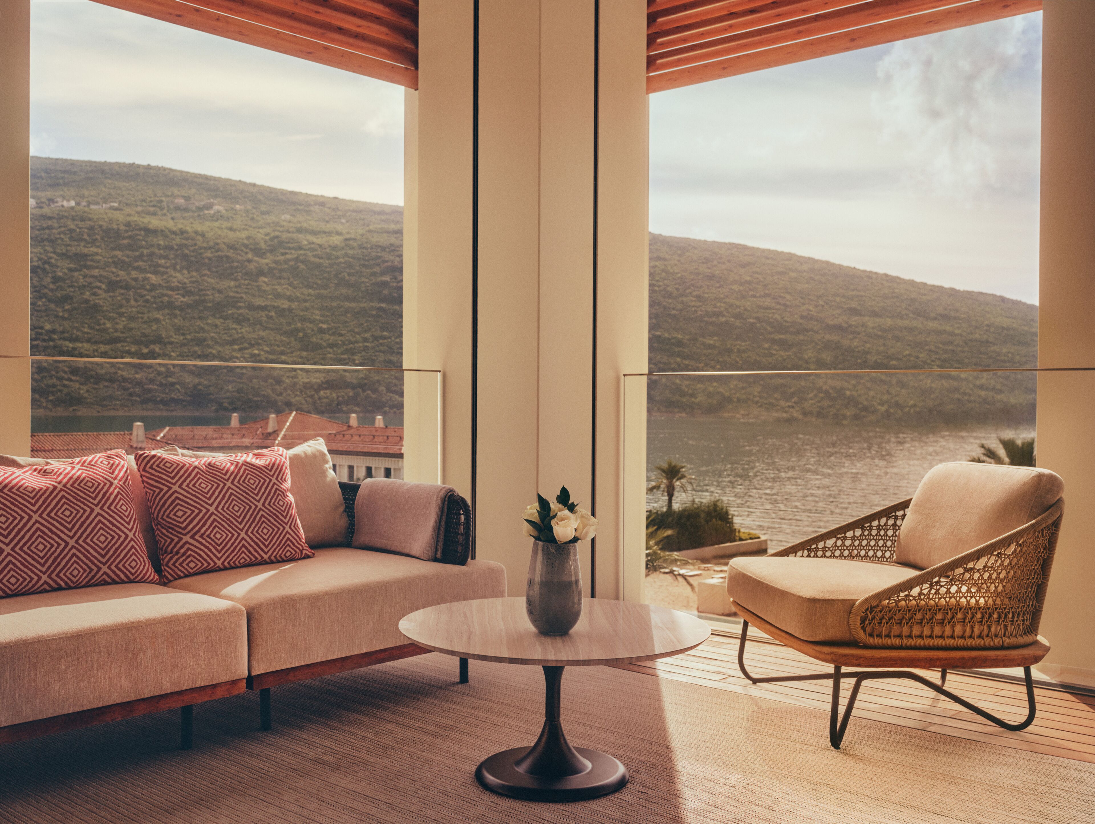 A balcony with a sofa, a chair, and a table, overlooking a body of water and hills.