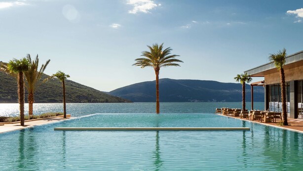 A clear blue sky, a swimming pool, palm trees, and a mountain in the background. - One&Only Portonovi (Kumbor)