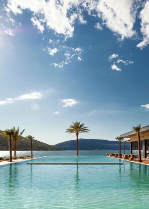 A clear blue sky, a swimming pool, palm trees, and a mountain in the background. - One&Only Portonovi (Kumbor)