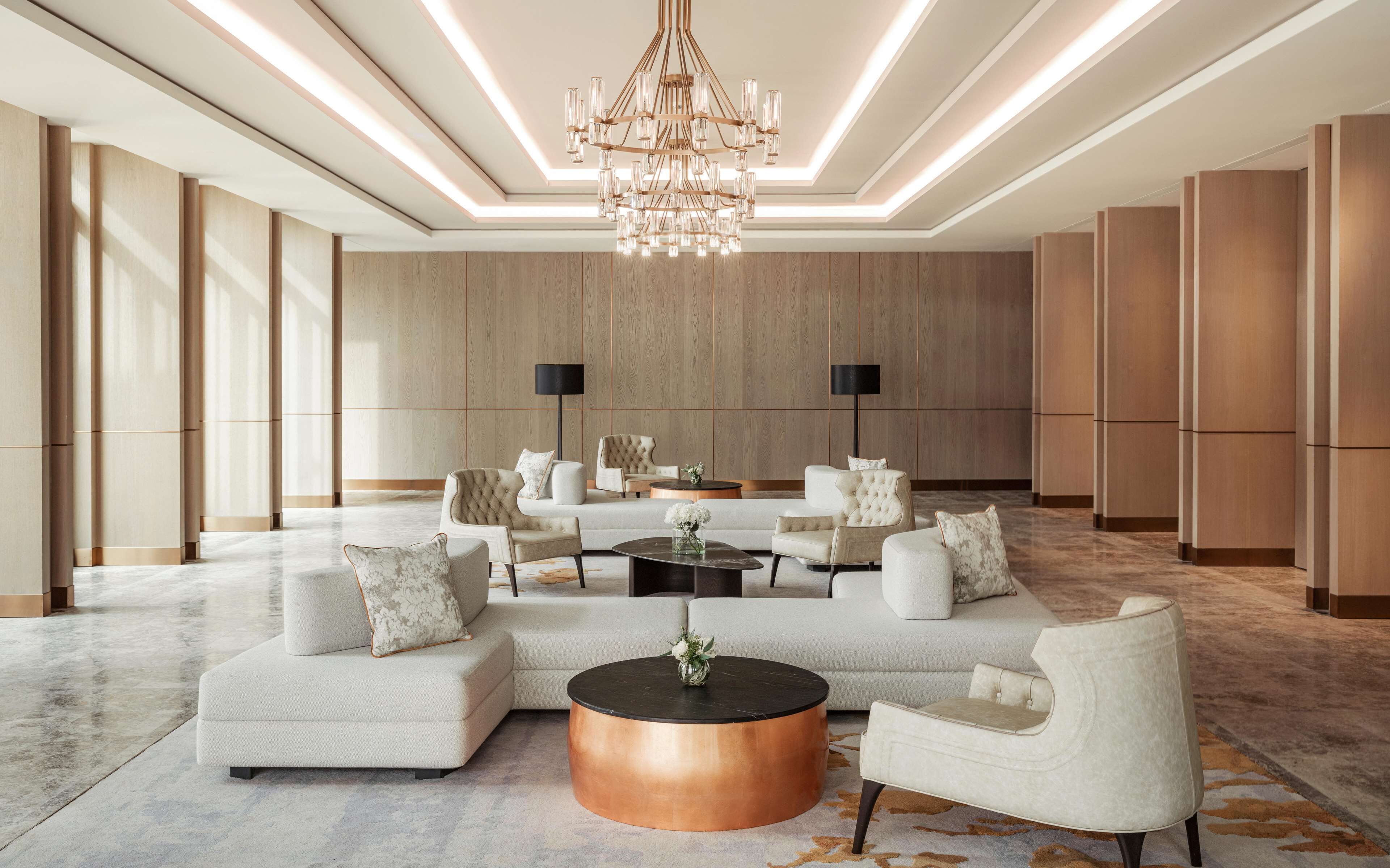 A spacious lobby with a large chandelier, a sectional sofa, and a round coffee table.