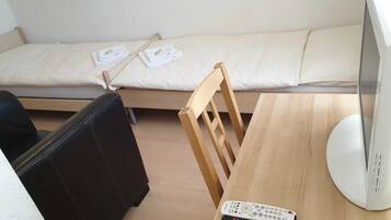 Una piccola stanza con un letto, un tavolo di legno, una TV e due telecomandi.