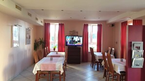 A dining area with a TV, red curtains, and a tiled floor. - Hotel Edelweiss (Neuhausen am Rheinfall)