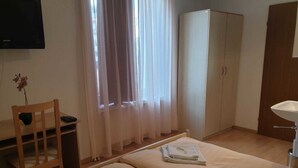 A hotel room with two beds, a wooden chair, a desk, a wardrobe, and a television on the wall. - Hotel Edelweiss (Neuhausen am Rheinfall)