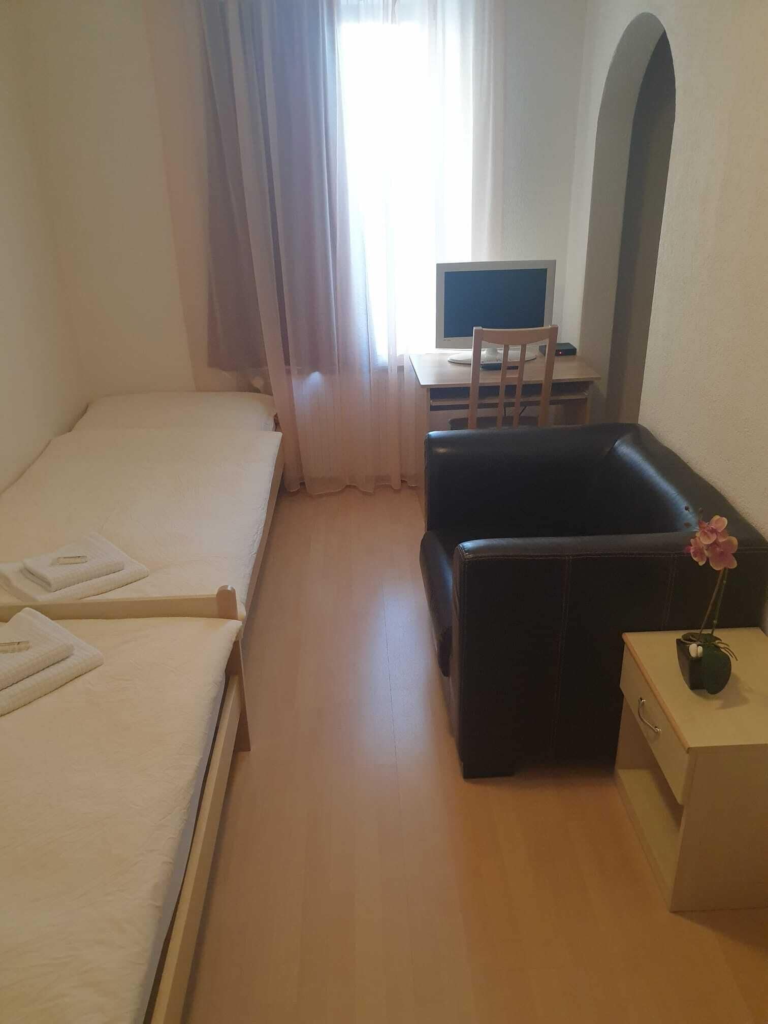 Een hotelkamer met een bed, een bureau met een computer, een zwarte bank en een klein nachtkastje met een bloevas.