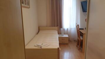 A bedroom with a bed, a bedside table, a chair, and a TV.