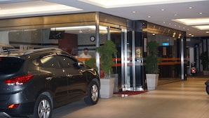 Una entrada de edificio moderna con un coche estacionado afuera, puertas de vidrio y plantas en macetas.