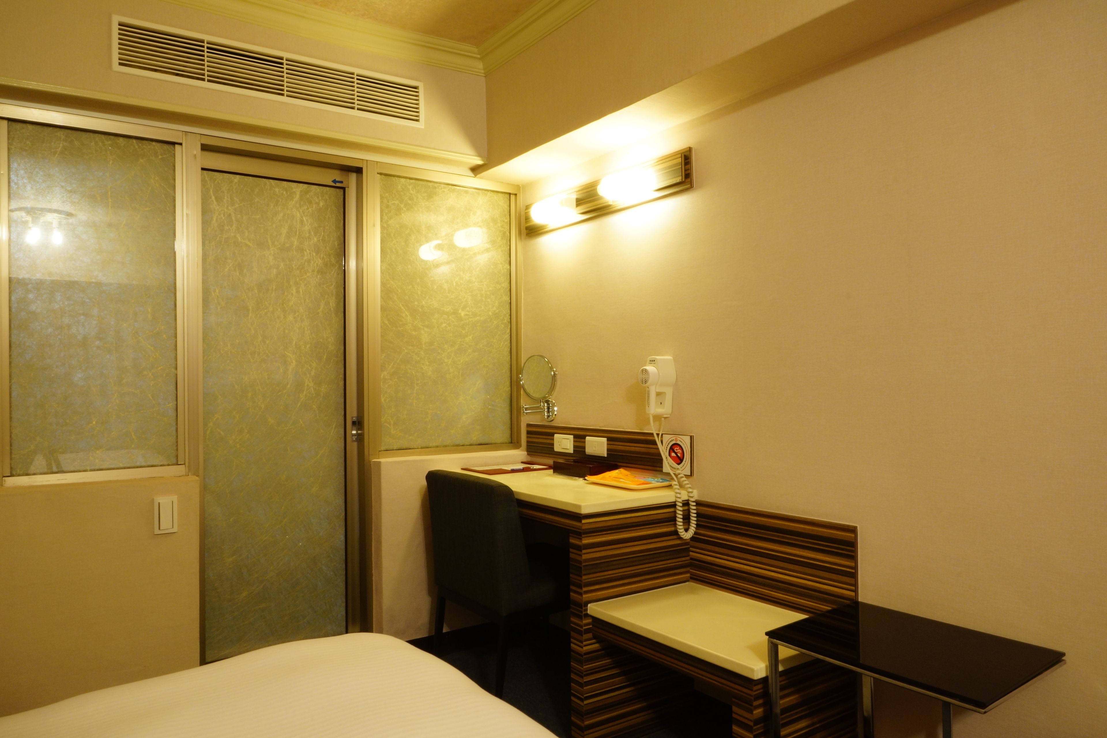 A hotel room with a bed, a desk with a chair, a mirror, and a telephone.