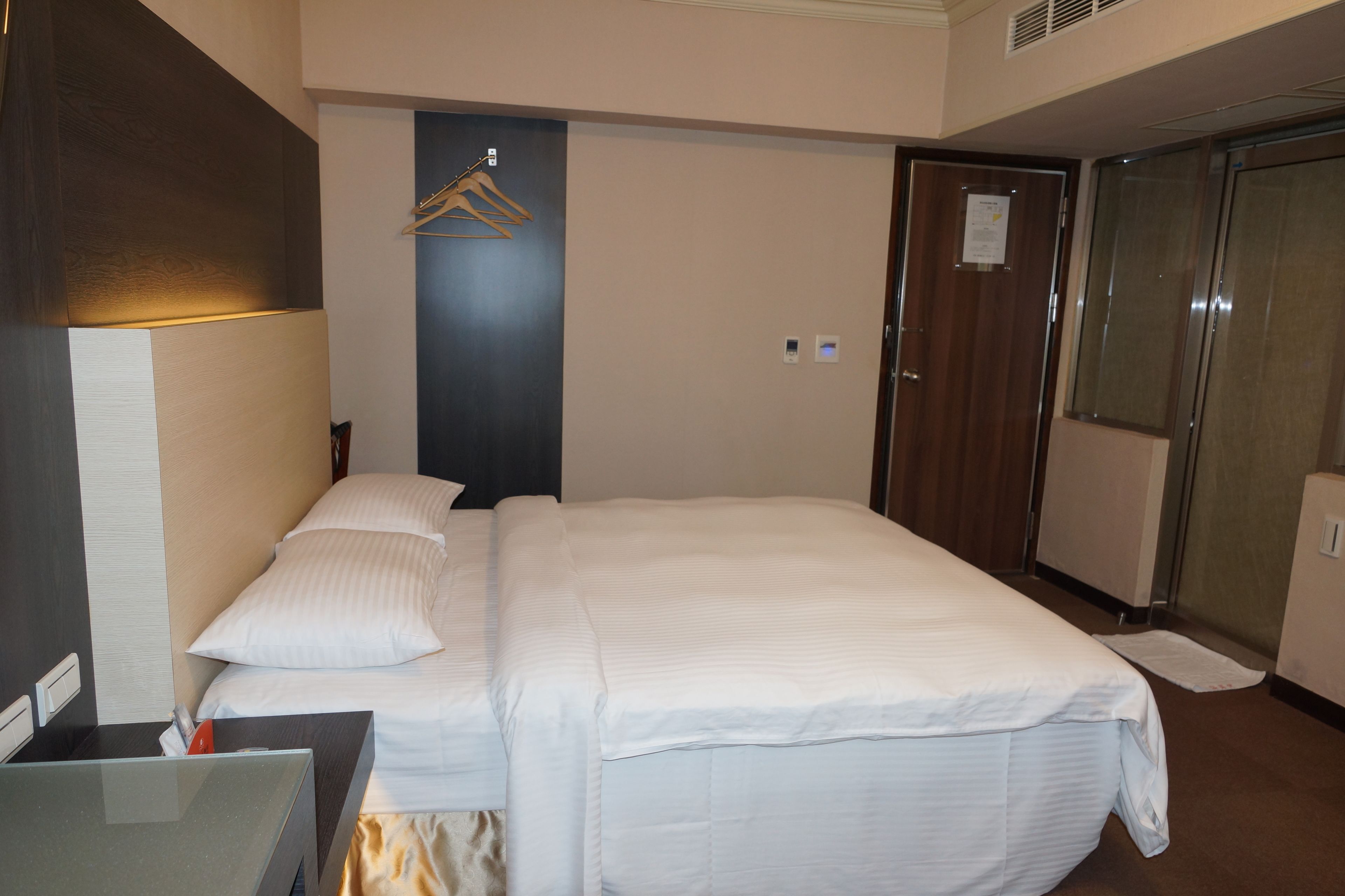 A hotel room with a bed, a desk, a mirror, a wardrobe, and a hanging coat rack.