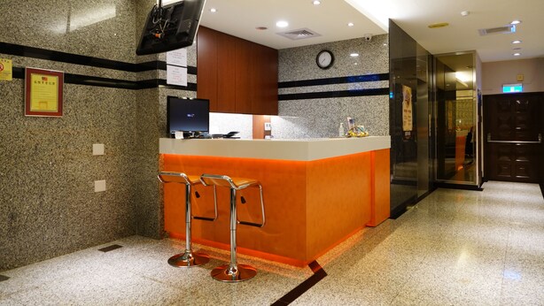 Zona de recepción de hotel con mostrador de granito, un reloj y una televisión montada en la pared.