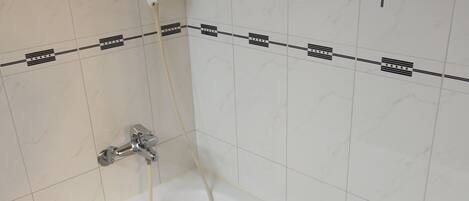 Un baño con una bañera blanca, ducha y suelo de baldosas.