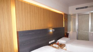 Habitación de hotel con dos camas, cabecero de madera, mesita de noche con teléfono y lámpara, y ventana con persianas.
