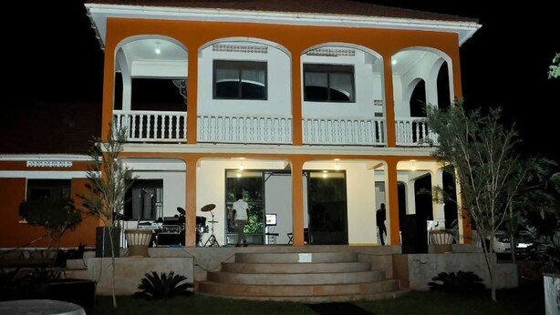 A two-story building with a balcony on the upper floor, a covered front porch, and a well-maintained lawn. - Dorabo Tourist Hotel (Jinja)