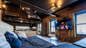 Un espacio habitable moderno estilo loft con cama alta, cocina, televisor y ventana grande con vista a la ciudad.
