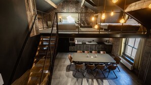 Una cocina moderna con comedor, que incluye una escalera, paredes de ladrillo visto e iluminación colgante.
