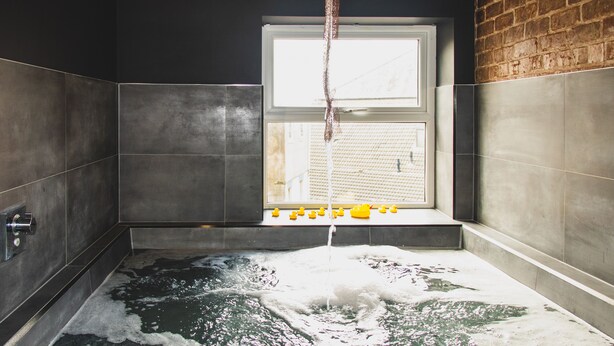 Una bañera con ventana, grifo y patitos de goma.