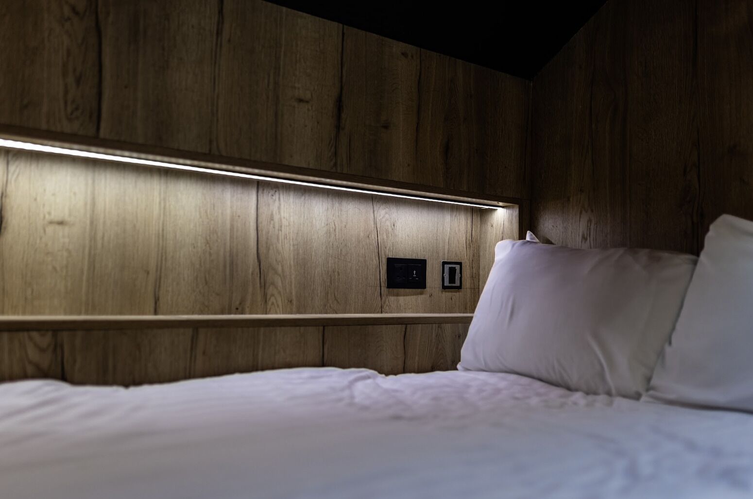 Een kamer met houten lambrisering, een bed, een nachtkastje en een wandlamp.